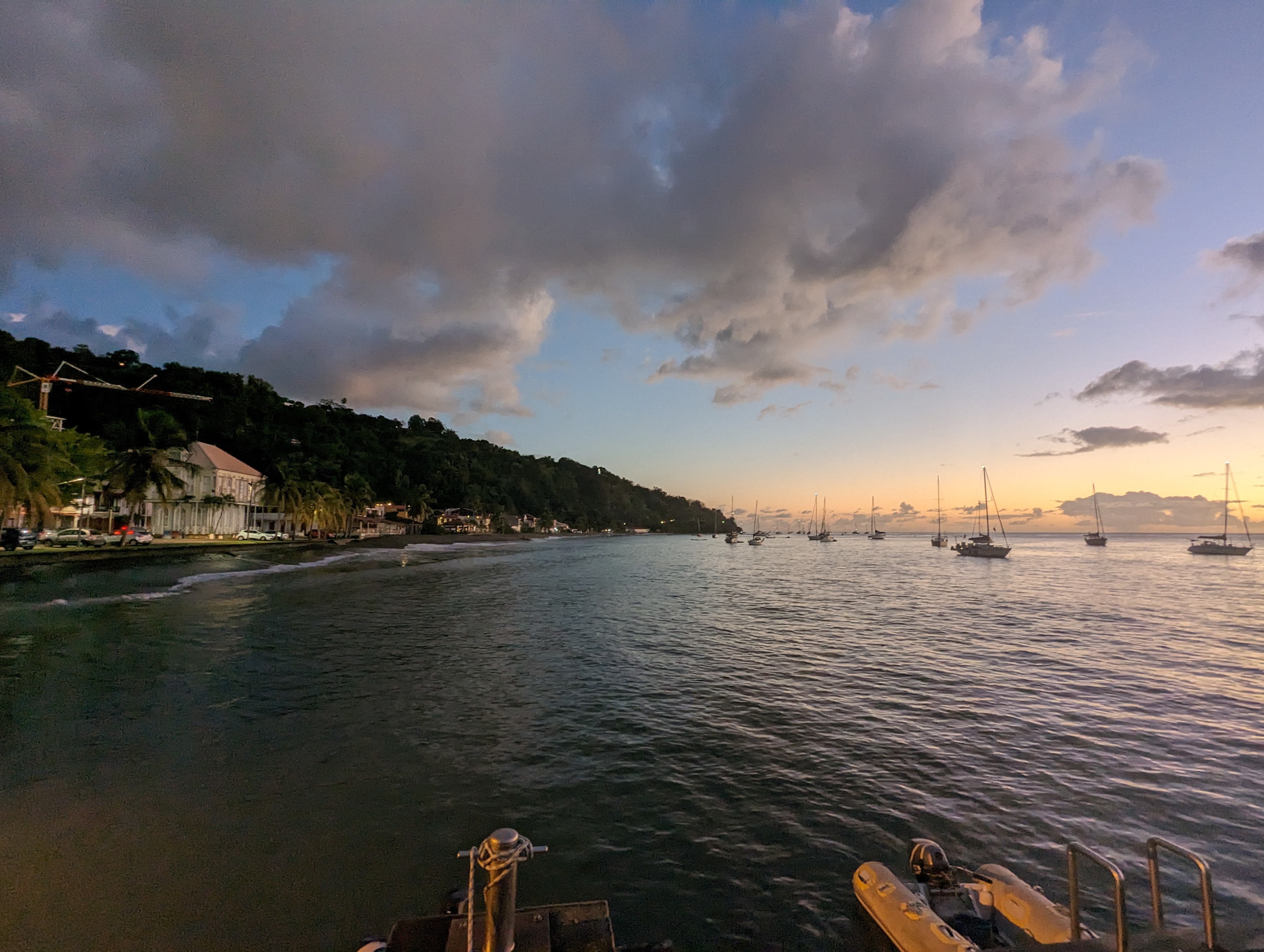 Martinique coastline with boats on the water, hillside buildings and clouds in evening light.
